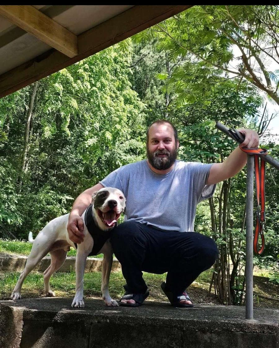 Travis Bollenbach crouched beside his dog on a stone wall